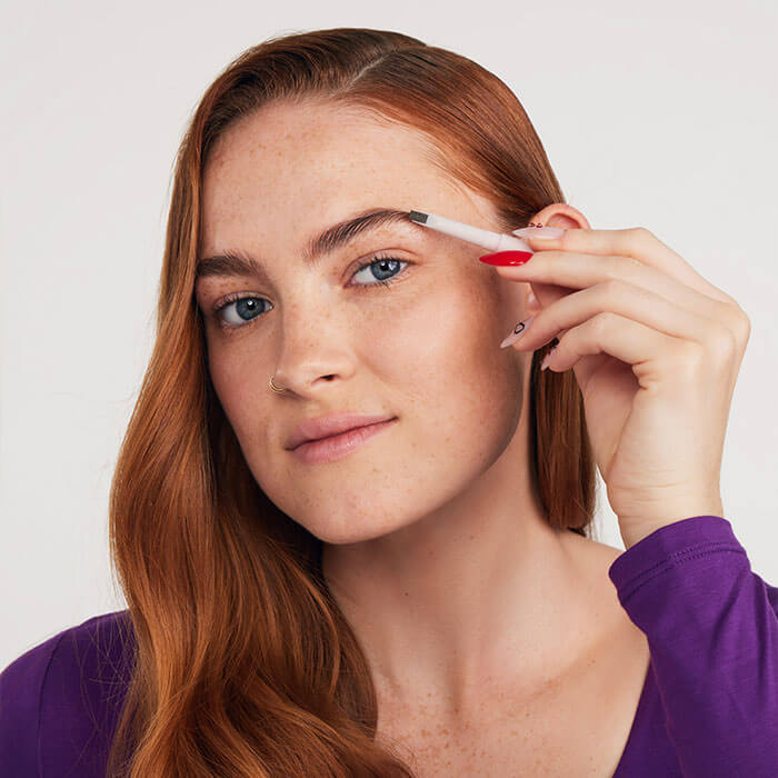 Woman with soft red hair tone skillfully using eyeshadow pencil to apply eyeshadow