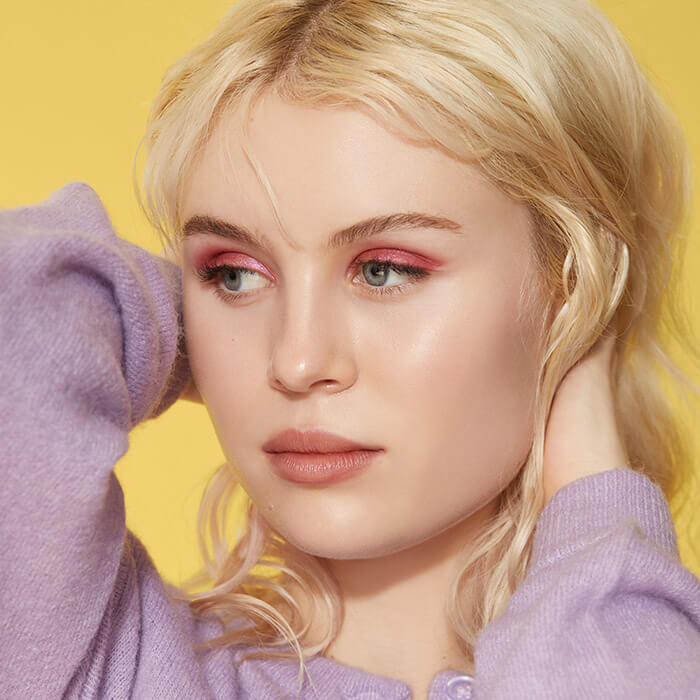 Blonde model posing and rocking a shimmery rose eyeshadow makeup look against yellow background