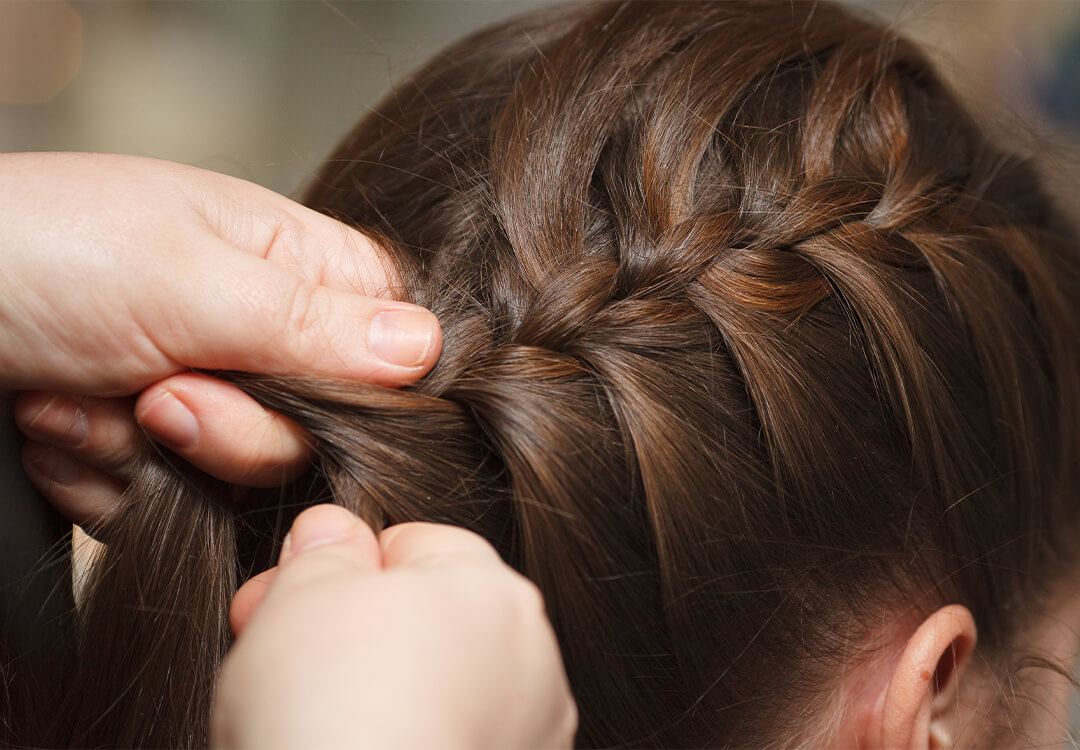 Close-up image of a woman's hair being braided by another woman's hands