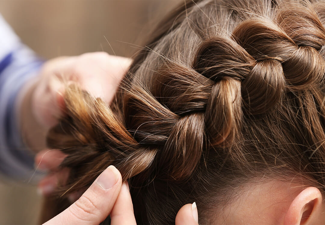 Close-up image of Dutch braids being done on a dark haired woman by another woman