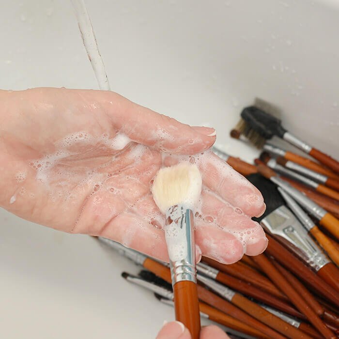 Close-up image of woman's hand cleaning brushes in the sink