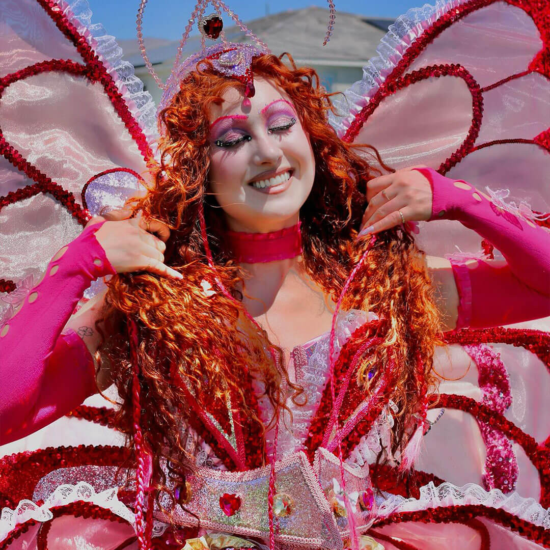 A vibrant and whimsical Halloween makeup look featuring a fantasy-inspired costume with red curls, intricate pink eye makeup, and butterfly wings