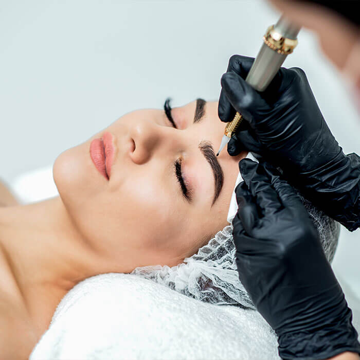 A professional beautician in black gloves carefully performs an ombré eyebrow procedure on a client with eyes closed and perfectly shaped brows, highlighting the precision and care that make this style so popular