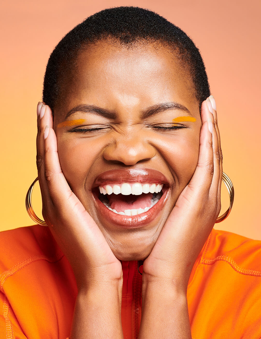 Closeup of a happy, excited and smiling African woman looking cheerful and beautiful while posing against an orange background. Face of one joyful, gorgeous and pretty black female
