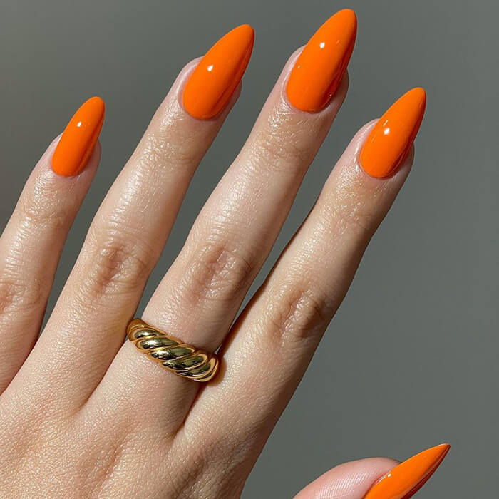 Close-up of woman's hand with gold ring and orange nail polish against dark grey background