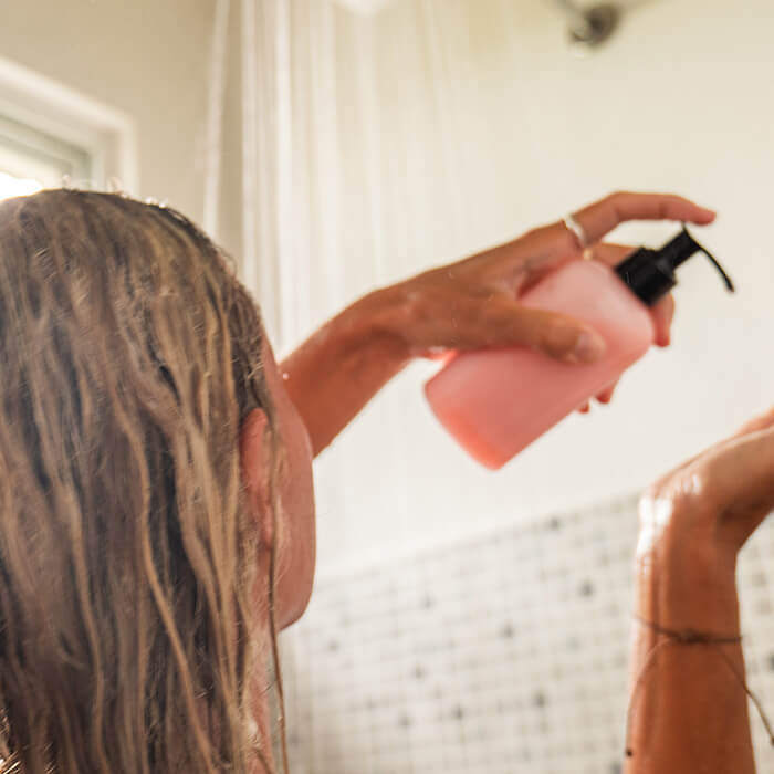 A photo of a woman taking a shower while pumping a pink bottle in a shower room