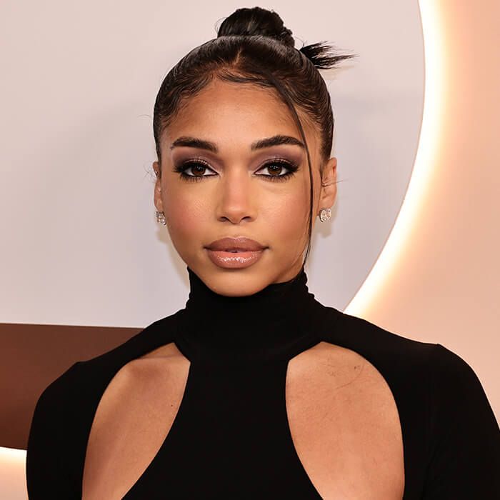 A photo of Lori Harvey with an espresso makeup look wearing a black dress on a beige background