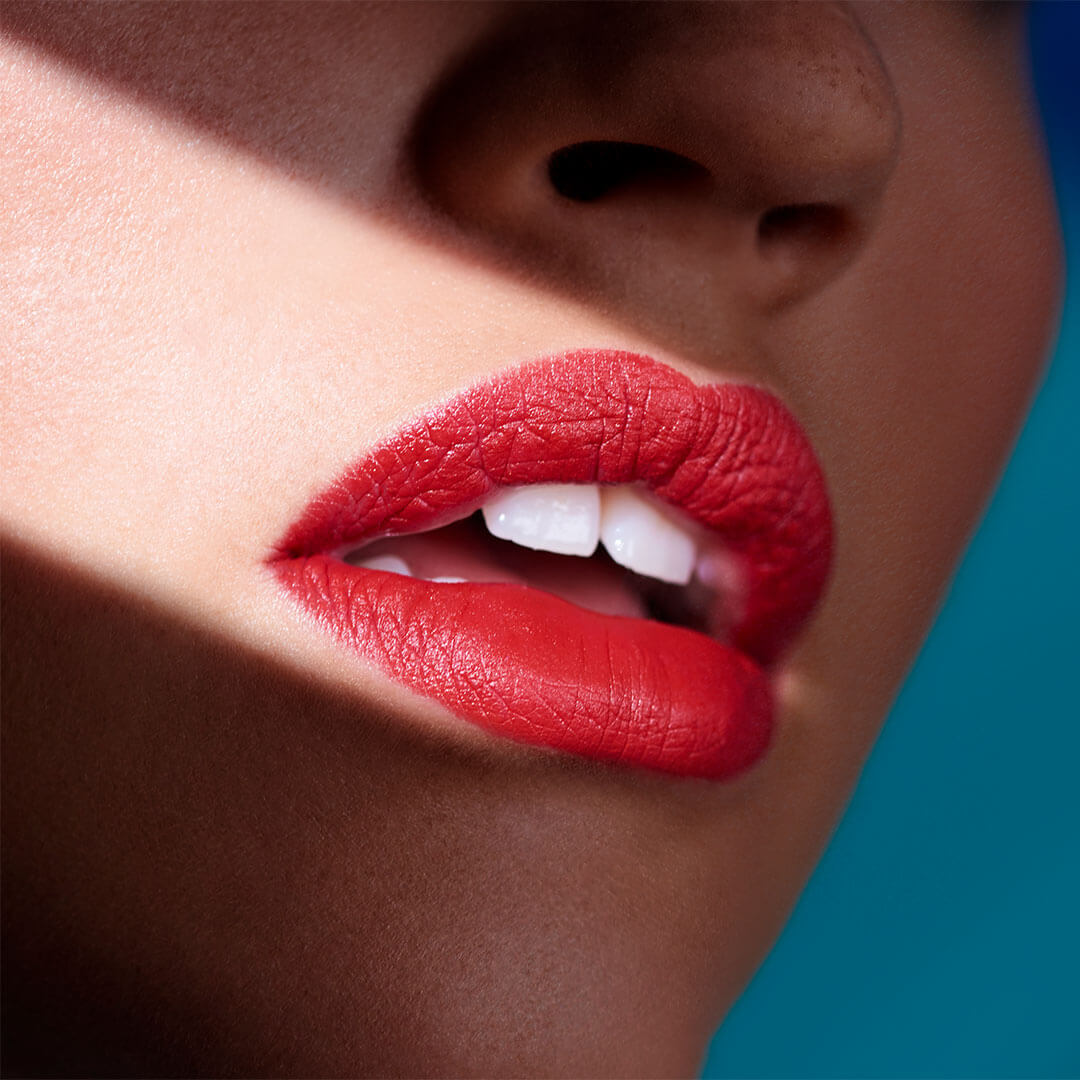 A close-up image of a woman's lips, painted in vibrant red lipstick, illuminated by a beam of sunlight