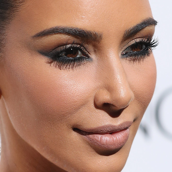 A photo of Kim Kardashian wearing a diamond waterdrop earrings, nude lipstick, and a black eyeliner