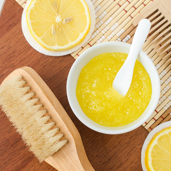 Homemade lemon fruit scrub in a small white bowl and wooden hair brush