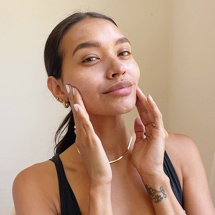 Close-up image of a model in black tank top touching her cheeks while smiling