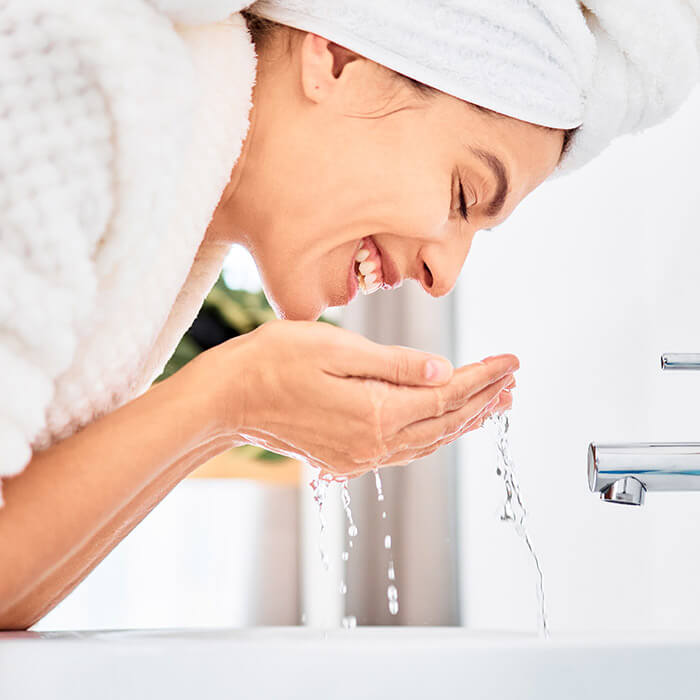 A photo of a model washing her face and smiling in the bathroom