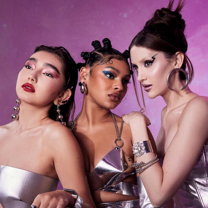 Three models with elaborate makeup posing in futuristic set