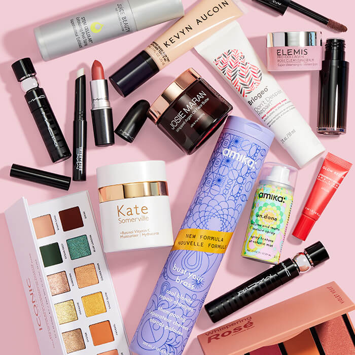 Beauty and makeup products from various brands scattered on pink background