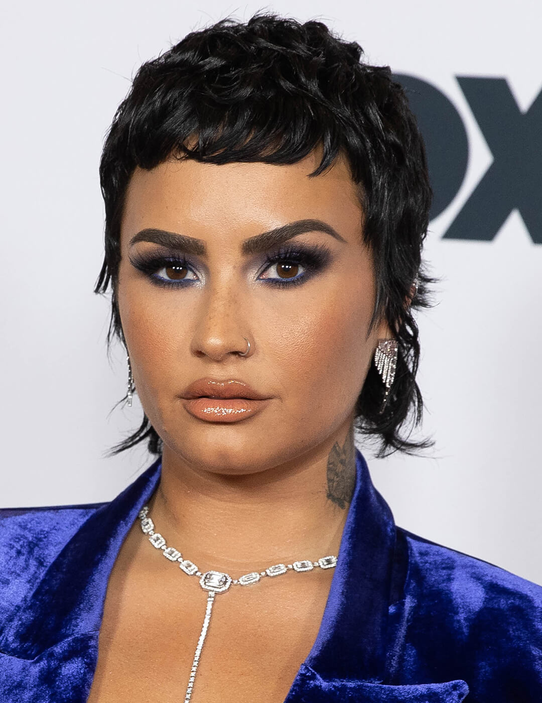Demi Lovato in a short mullet, blue suede suit, and smoky eye makeup look