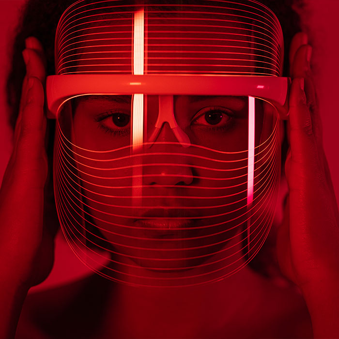 A close-up image of a woman wearing a red-light therapy mask while situated in a room illuminated with red lighting