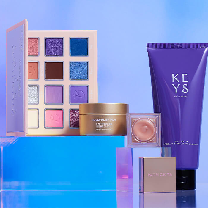 Makeup and beauty products from various brands on clear acrylic cubes against light blue background