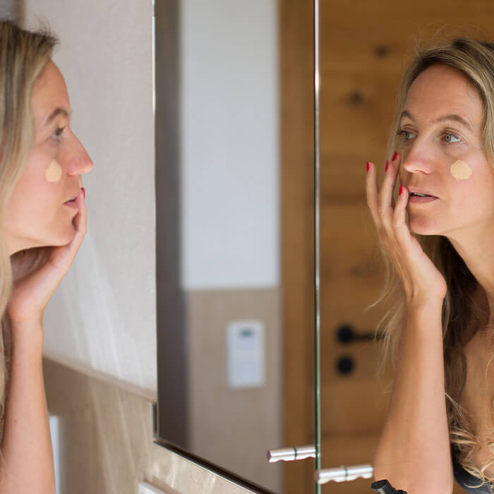 A photo of a model applying foundation in front of bathroom mirror