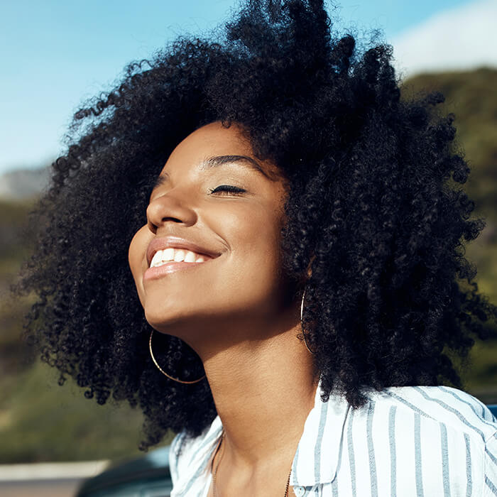 Close-up of a woman of color smiling in the sun against greenery background