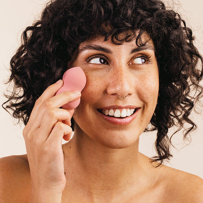 An image of a women using a pink sponge to apply something to her face