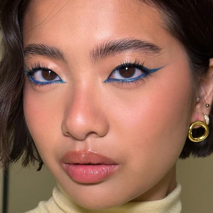 A close-up image of a woman wearing a blue-colored winged eyeliner