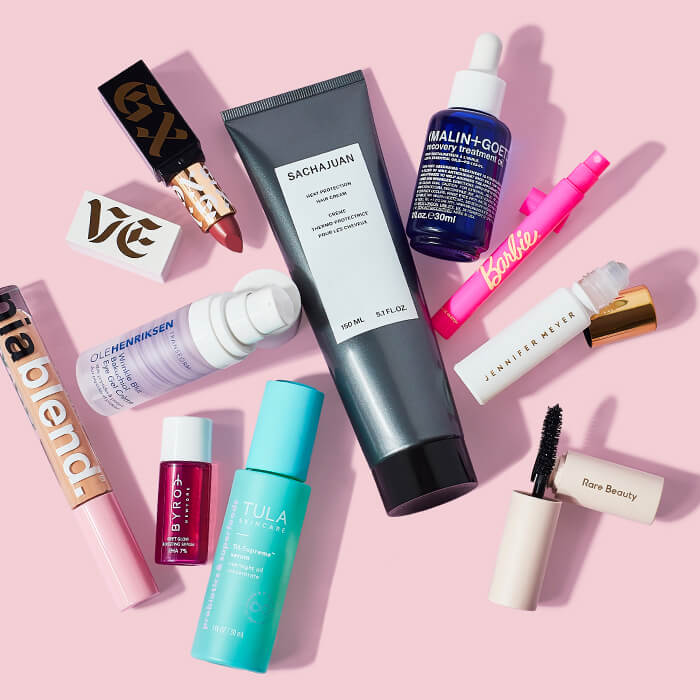 Skincare and makeup products from various brands scattered on pink background