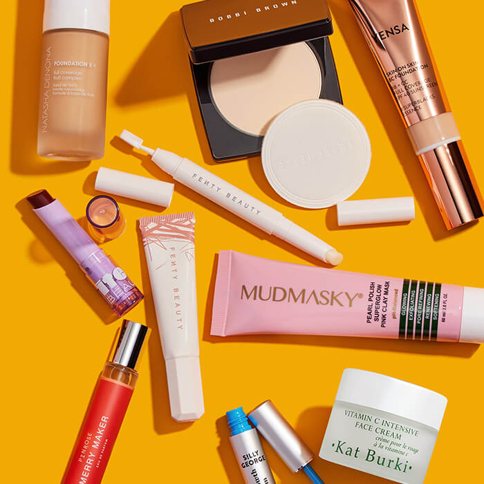 Makeup, skincare, and beauty products and tools from various brands scattered on orange background