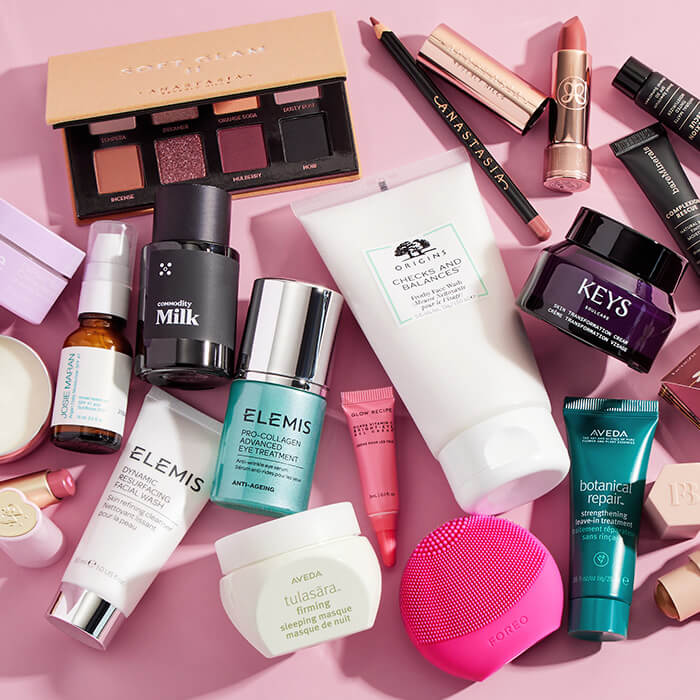 Beauty and makeup products from various brands scattered on pink background