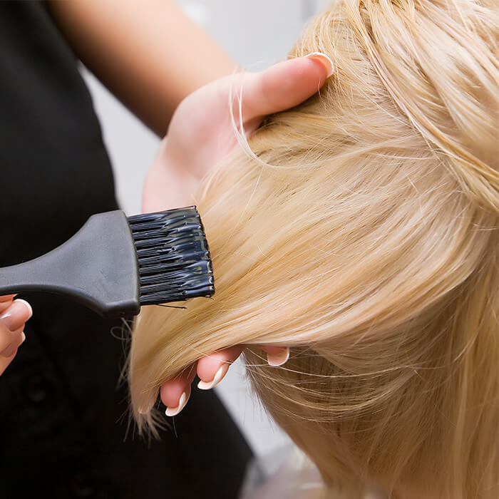 Close-up of a hair colorist applying product on a woman's blonde hair using a brush