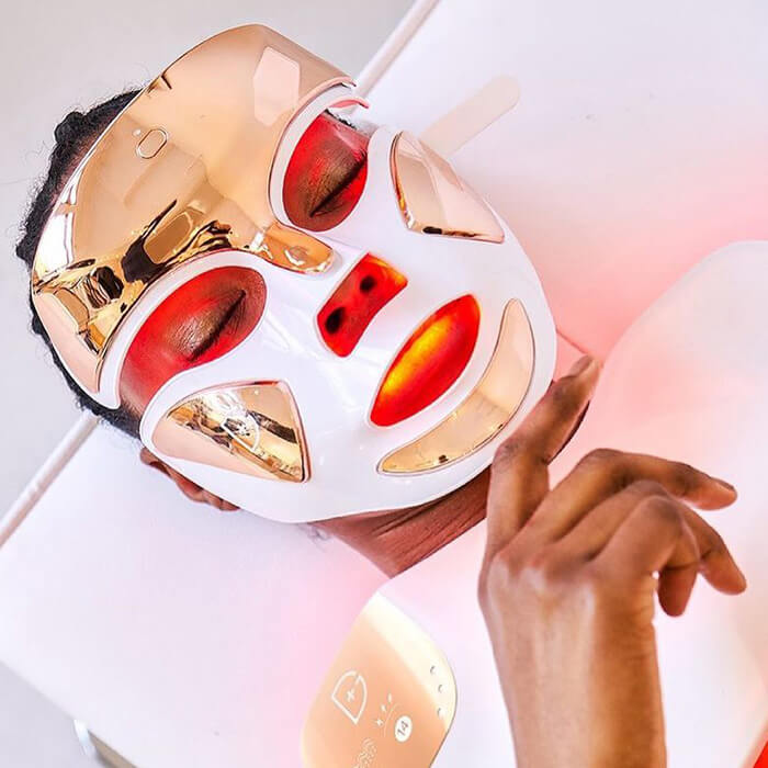 A photo of a model laying on bed using the DR. DENNIS GROSS SKINCARE DRx SpectraLite FaceWare Pro LED Face Mask