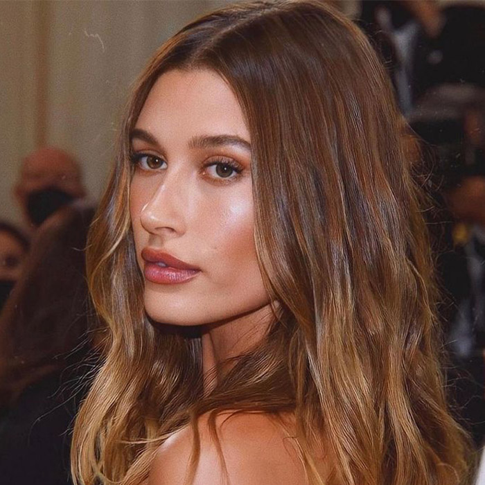 A sideview image of Hailey Bieber showing her balayage hair paired with brown-toned makeup