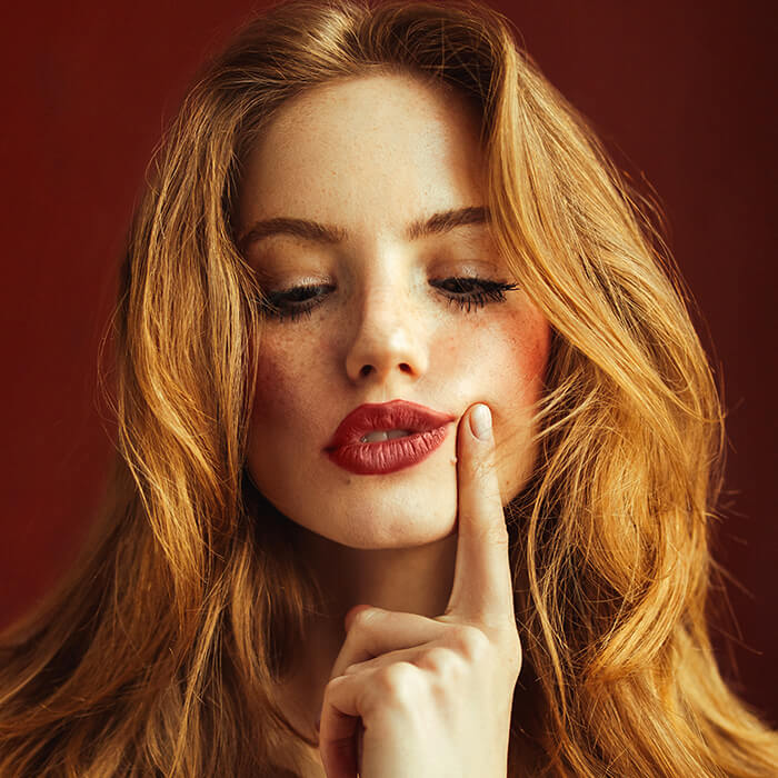 A photo of a woman with red hair and nude makeup look pressing her finger on cheeks