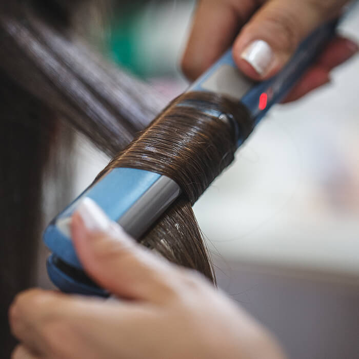 Close-up image of a hairstylist's hands using a flat iron to curl a woman's dark hair