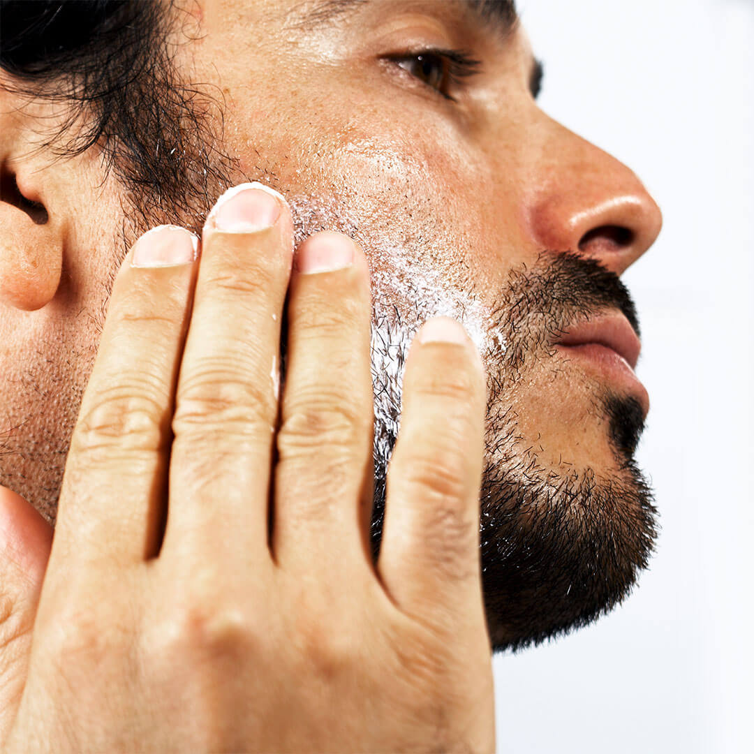 A detailed side profile of a man gently rubbing a cream into his slightly bearded skin