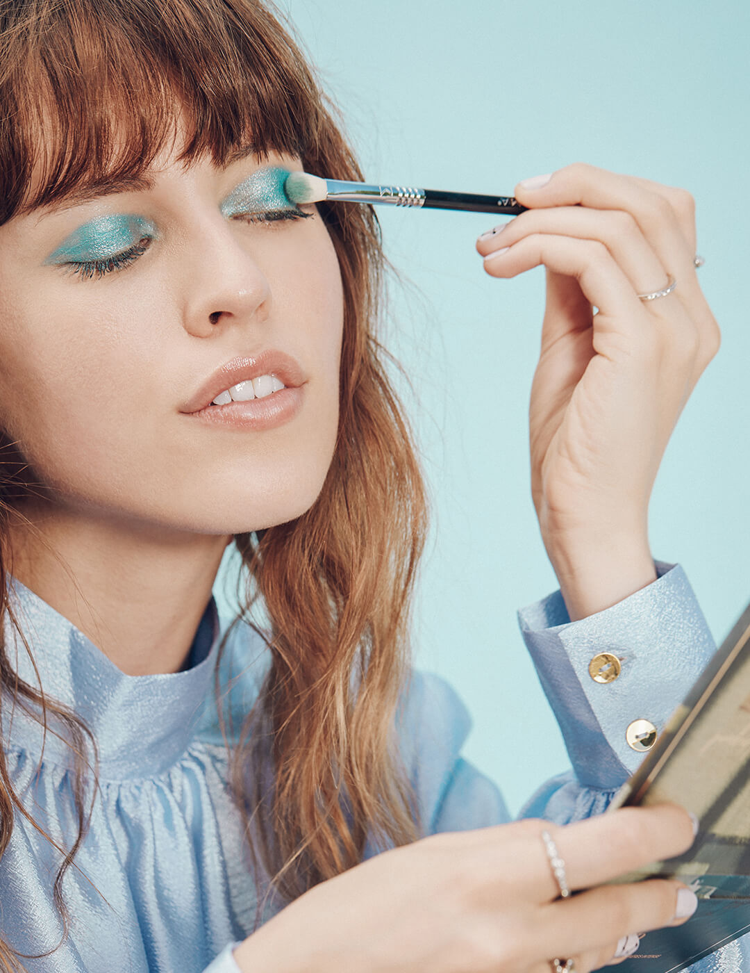 An image of a model putting shimmery blue eyeshadow with a makeup brush