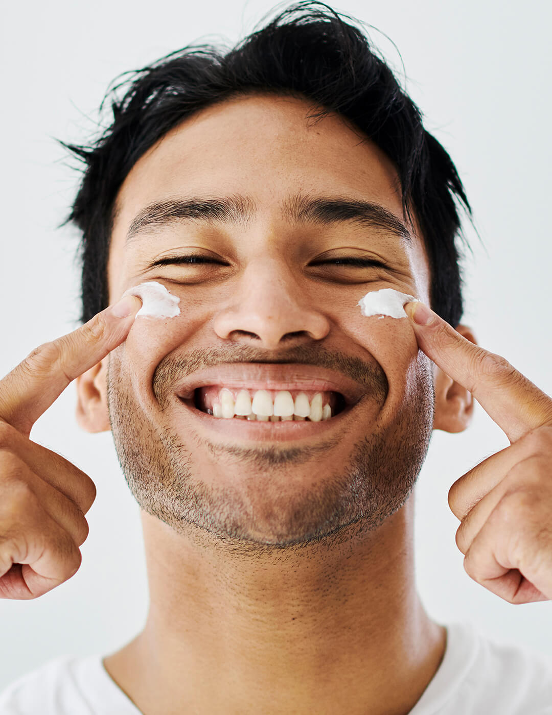 Man grooming, applying face cream or lotion, enjoying self care against grey background with copy space. Guy smiling while doing treatment and skincare. Male trying an anti aging or hydrating facial