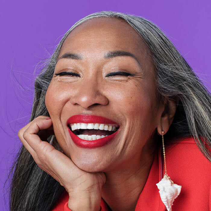 A photo of a mature woman laughing wearing a red lipstick over a purple background