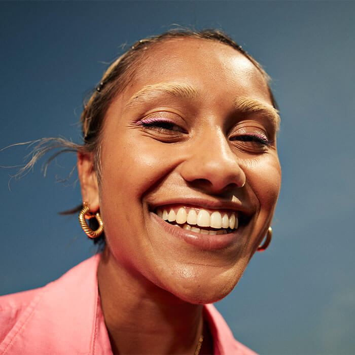 Joyful woman with a toothy grin, vibrant skin, and stylish facial traits contrasted with the sky in a close-up portrait