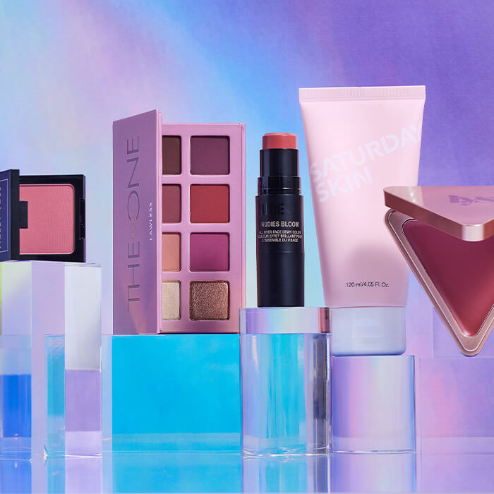 Beauty products from various brands on clear acrylic cubes against gradient light blue and purple background