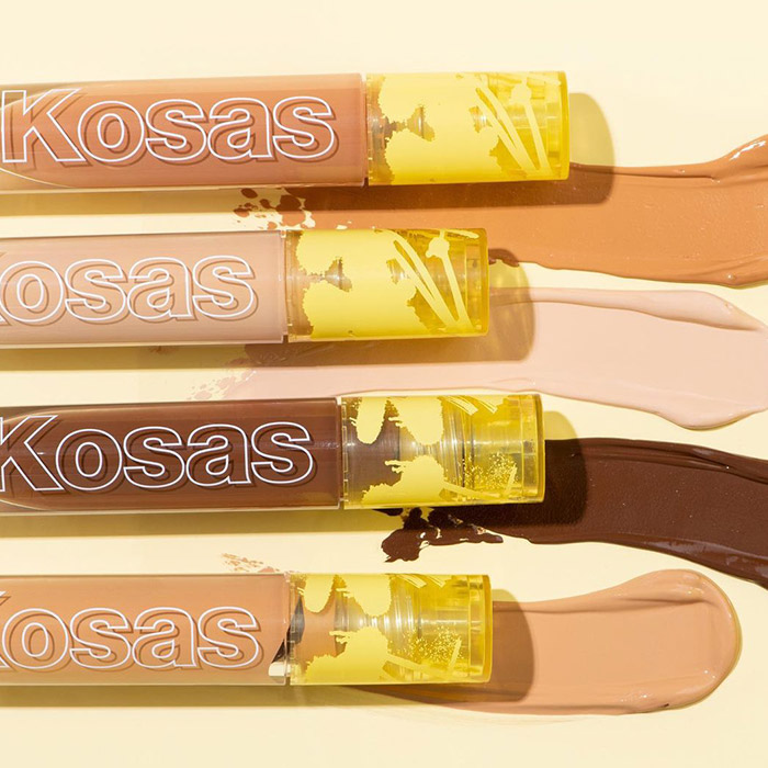 A photo of different shades and swatches of KOSAS Revealer Concealer on a yellow background