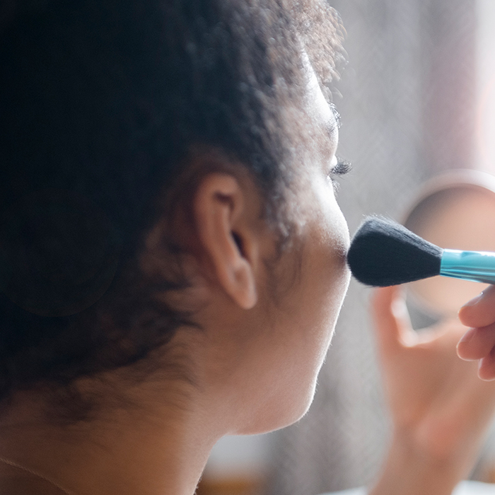 A closeup shot of a woman applying makeup with a brush on her cheeks