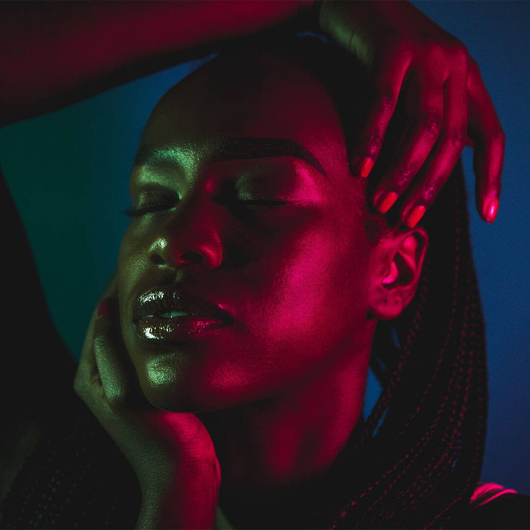 A photo of a woman with her eyes closed, bathed in green and red light effects within a dark studio setting