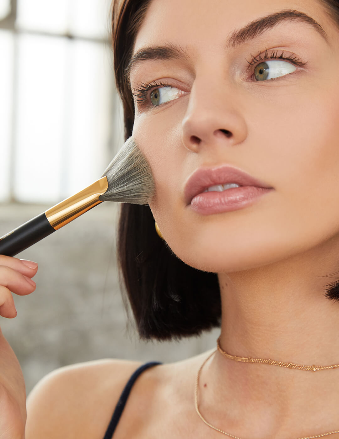 An image of a model touching her cheek with a makeup brush