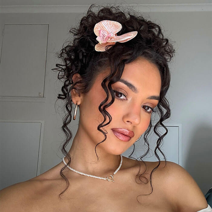 Close-up of a woman with voluminous curls and face-framing tendrils, featuring a soft, floral accent in her hair