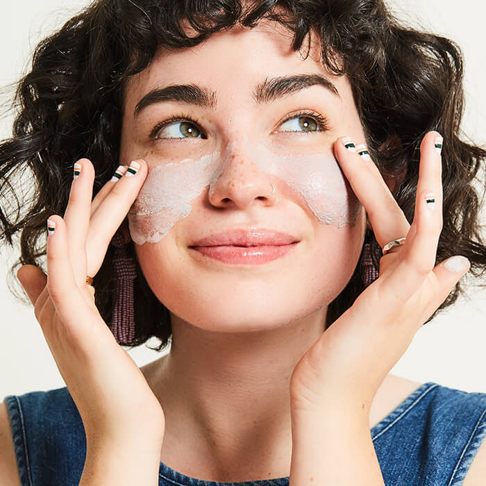 An image of a happy woman applying facial cream on her face