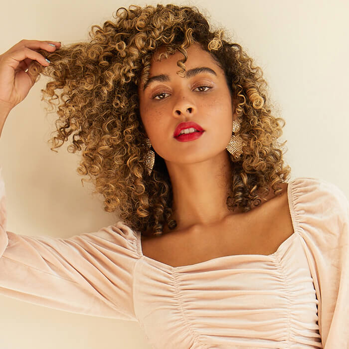 Image of a curly-haired model with neutral eye makeup and bold red lips posing and holding her hair