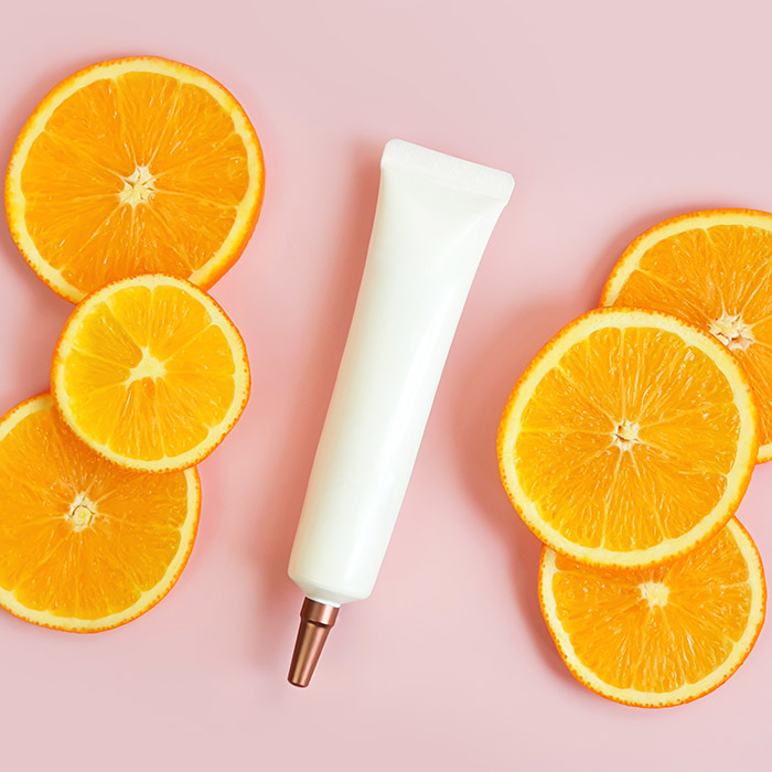 A photo of a serum with orange slices on a pink background