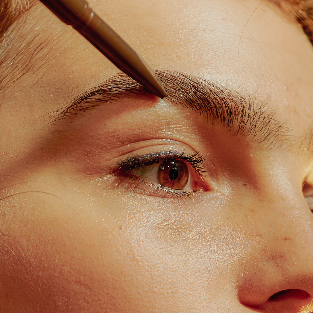Close-up of a young woman applying eyebrow pencil on her brows