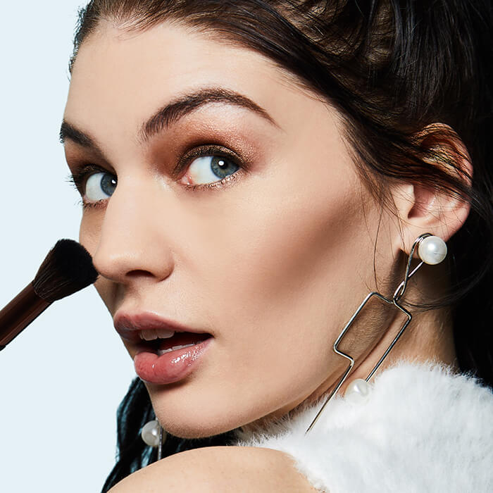 An image of a woman holding a makeup brush while showing her defined cheekbone and glittery eyeshadow