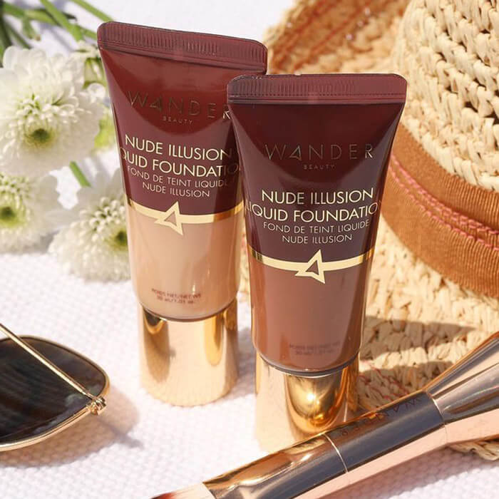 Two tubes of WANDER BEAUTY Nude Illusion Liquid Foundation in different shades with straw hat, white flower, sunglasses, and makeup brush